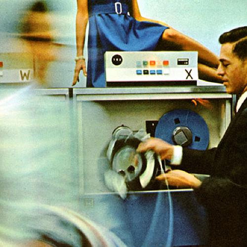Annual Reports and Corporate Communications depicts: A woman in a blue dress sits on top of a machine, beneath her two men feed some sort of reel or tape into the machine  