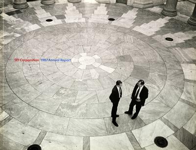 Annual Reports and Corporate Communications depicts: Two men in suits stand on a circular patterned tile floor, they are seen from above 