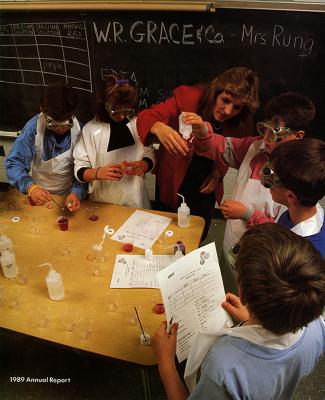Annual Reports and Corporate Communications depicts: A teacher and five young students perform a scientific experiment at a wooden table in front of a blackboard 