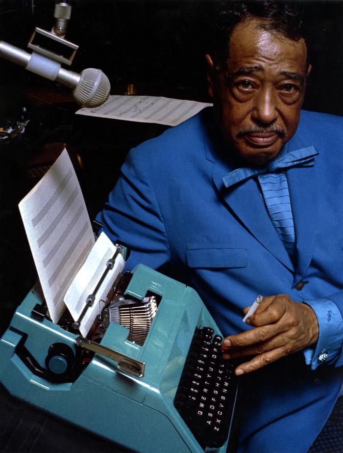Photographic Materials, Photographic Materials depicts: Duke Ellington is wearing a blue suit and smoking a cigarette, he types on a blue typewriter, on the pages are the lines for sheet music 