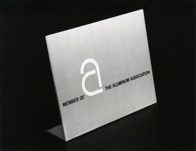 Photographic Materials, Logos and identities depicts: A large white lower case "A" is on a gray plaque of paper, it is in the middle of the phrase "Member of The Aluminum Association," the plaque is seen from the side 