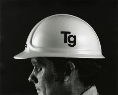Profile of a man wearing a white hardhat with the letters "TG" printed on it 