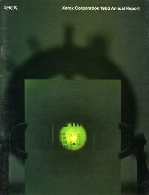 Annual Reports and Corporate Communications depicts: Out of focus dark green background with a circular shadow on the wall, and in front a green tinted sheet of paper with a lime green light shining in the middle. The paper is being held by two low tech mechanical hands, with white text at the top of the image.