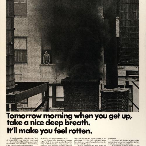 Man looks out a window to see a chimney with a plume of black smoke coming out 