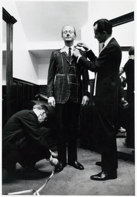 Photographic Materials depicts: Black and white photo of man being fitted for a suit jacket by two tailors