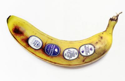 Posters depicts: Browning banana with four fruit stickers on it 