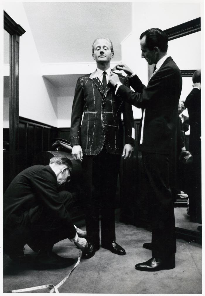 Photographic Materials depicts: Black and white photo of man being fitted for a suit jacket by two tailors