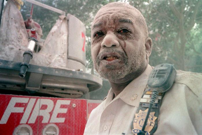 Photographic Materials depicts: Man, from shoulders up, in uniform standing next to fire truck, covered in dust