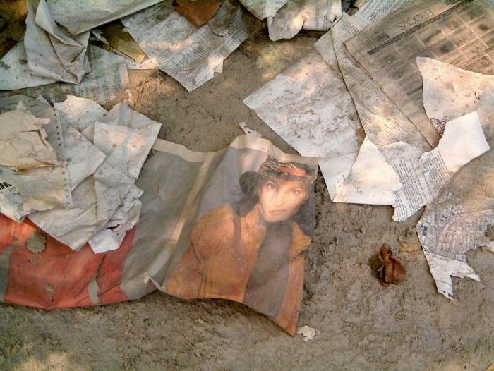Photographic Materials depicts: Documents and newspaper sheets scattered along the ground, with one spread open to a woman's face