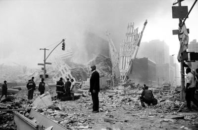 Photographic Materials depicts: A man in a business suit stands in front of the rubble of the twin towers, with police, firefighters, and a photographer in the background