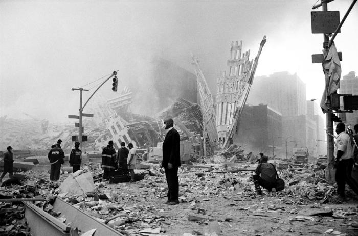 Photographic Materials depicts: A man in a business suit stands in front of the rubble of the twin towers, with police, firefighters, and a photographer in the background