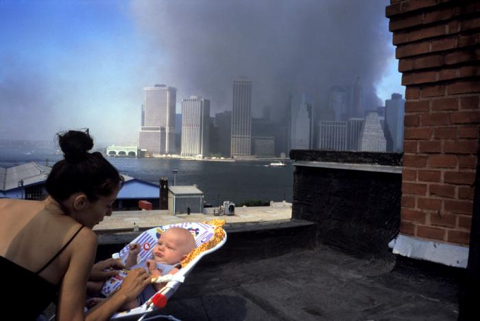 Photographic Materials depicts: Woman with baby in foreground, downtown Manhattan with large smoke plume in background