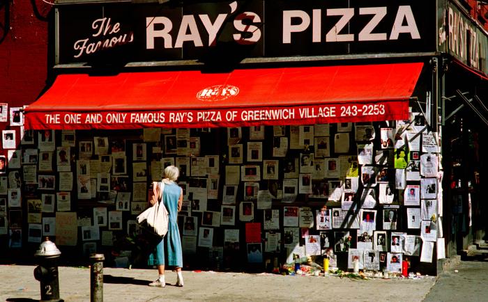 Photographic Materials depicts: Woman looking at the exterior of Ray's Pizza covered in flyers for missing people 