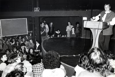 Photographic Materials depicts: black and white photograph of Martin behind lectern on stage surrounded by audience
