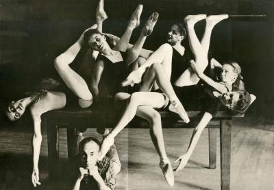 Serial Publications depicts: Black and white photo of a smiling man under a table with ballet dancers spread across it