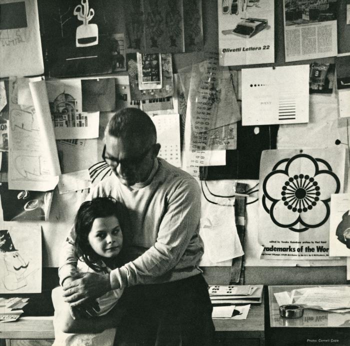 Announcements and invitations depicts: Photograph of Paul Rand in his studio hugging a child