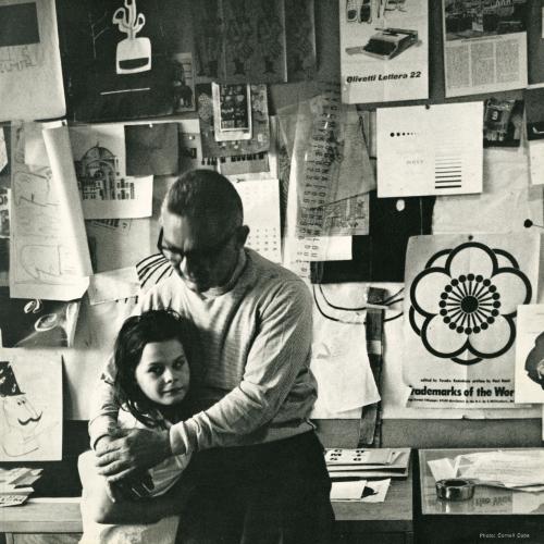 Announcements and invitations depicts: Photograph of Paul Rand in his studio hugging a child