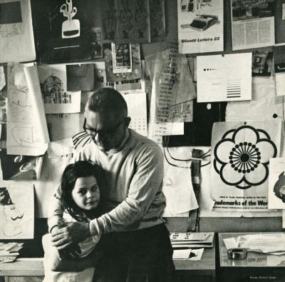 Announcements and invitations depicts: Photograph of Paul Rand in his studio hugging a child
