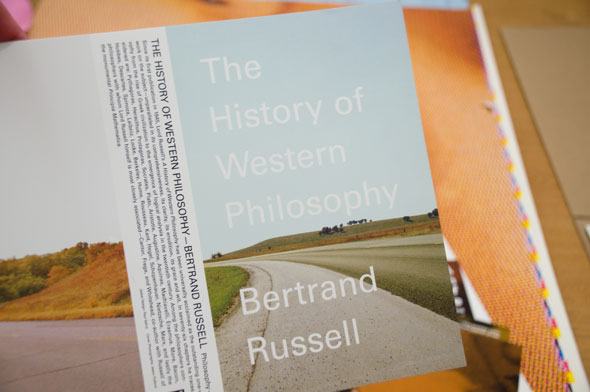 A photo of a book jacket for "The History of Western Philosophy" by Bertrand Russell.The title and author's name is written in a thin white front. The front is a picture of an empty road in plain calm field. 