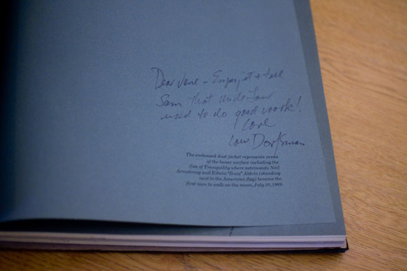 Book opened to show blue inner pages with dark blue cursive writing in lower right corner