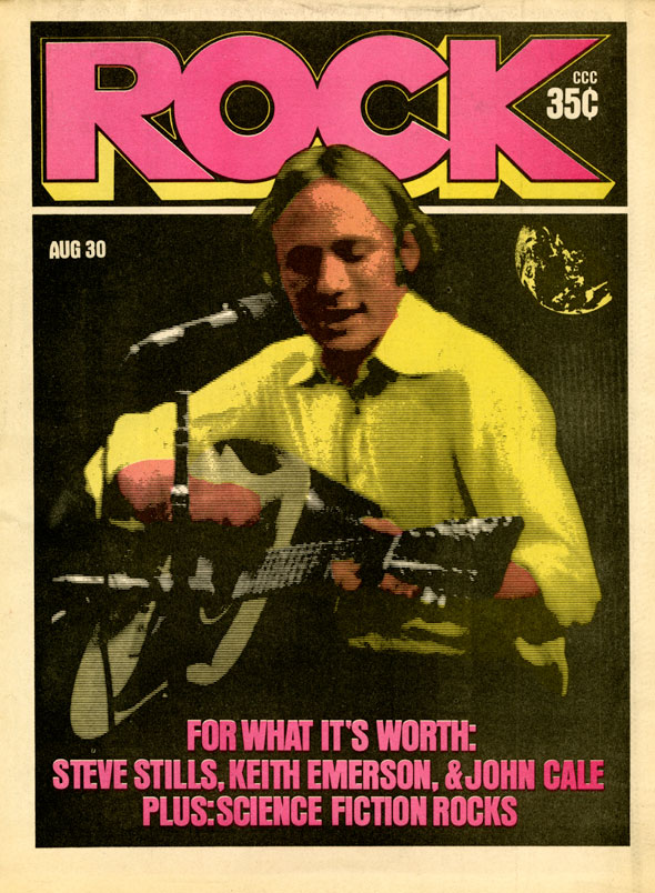 Magazine cover; colored photograph of a man in a yellow shirt playing guitar and singing into a microphone. Text and header are in bright pink